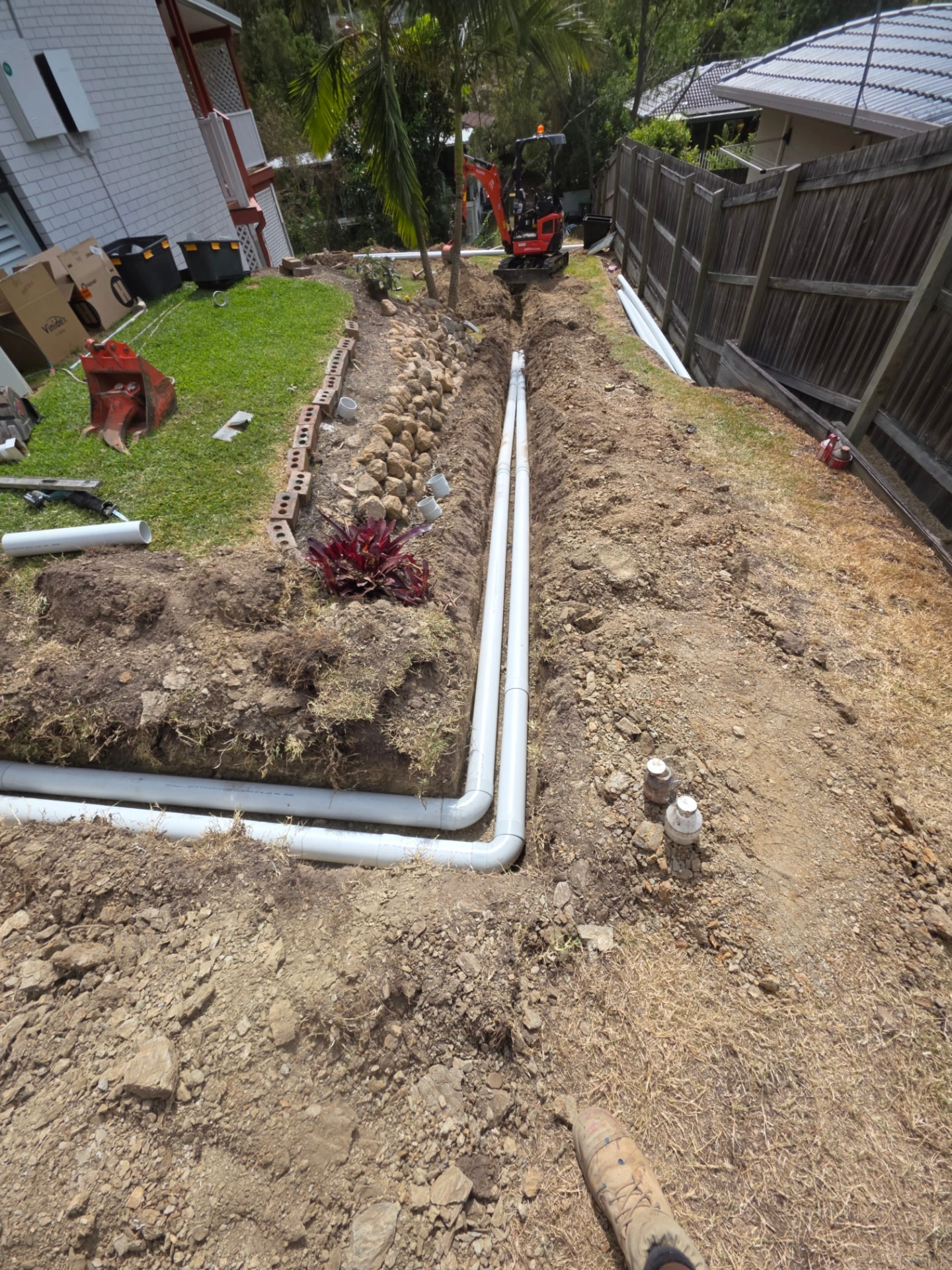 New PVC drainage pipework laid in an excavated trench beside a Brisbane home