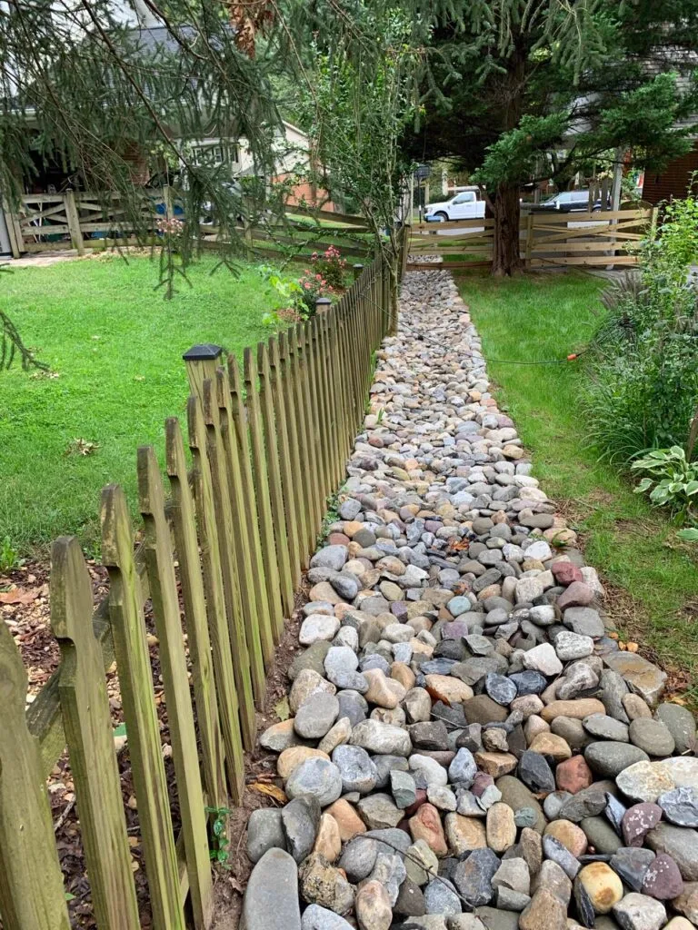 River-stone spoon drain running along a garden fence line, Brisbane spoon drains